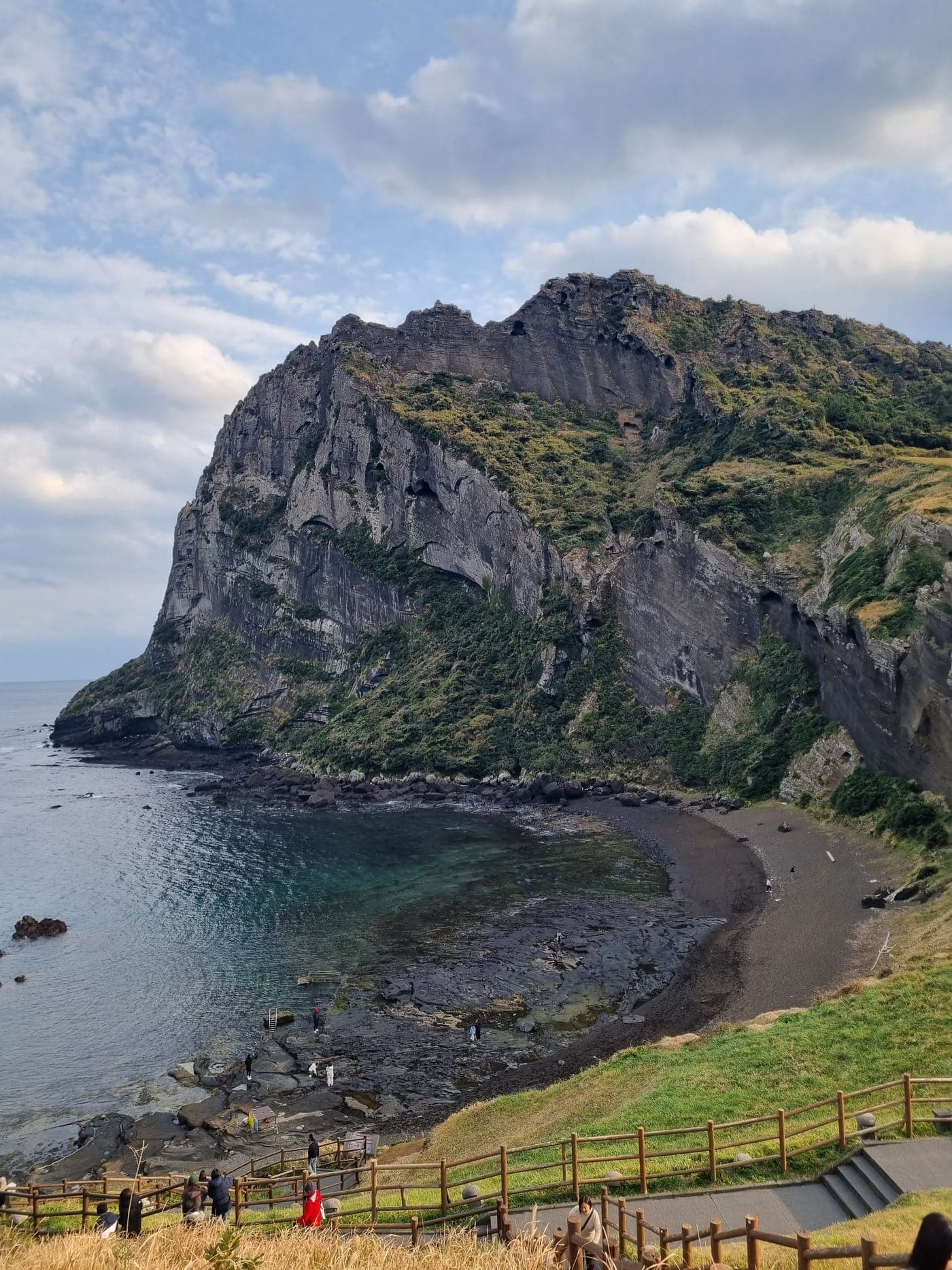 Seongsan Ilchulbong's ridge and cliffs rising above the sea, with an emerald cove below